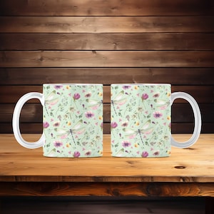 Op de afbeelding: Twee witte keramische mokken met een groene achtergrond en een herhalend patroon van roze en paarse bloemen, groene bladeren en witte libellen.