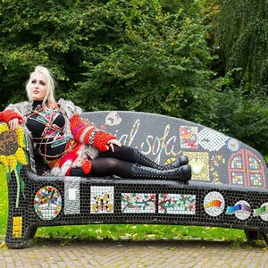 May include: A black mosaic sofa featuring colourful tile patterns including a sunflower, a butterfly, and floral designs. The backrest displays the text "social sofa" in white script. The sofa is constructed with small black tiles.