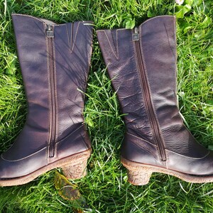 Side view of El Naturalista dark brown leather boots with zippers, displayed on green grass, highlighting their durable design and cork-textured heels.