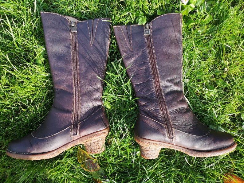Side view of El Naturalista dark brown leather boots with zippers, displayed on green grass, highlighting their durable design and cork-textured heels.