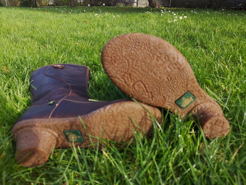 El Naturalista dark brown leather boots lying on green grass, highlighting their unique textured soles and eco-friendly frog logo.