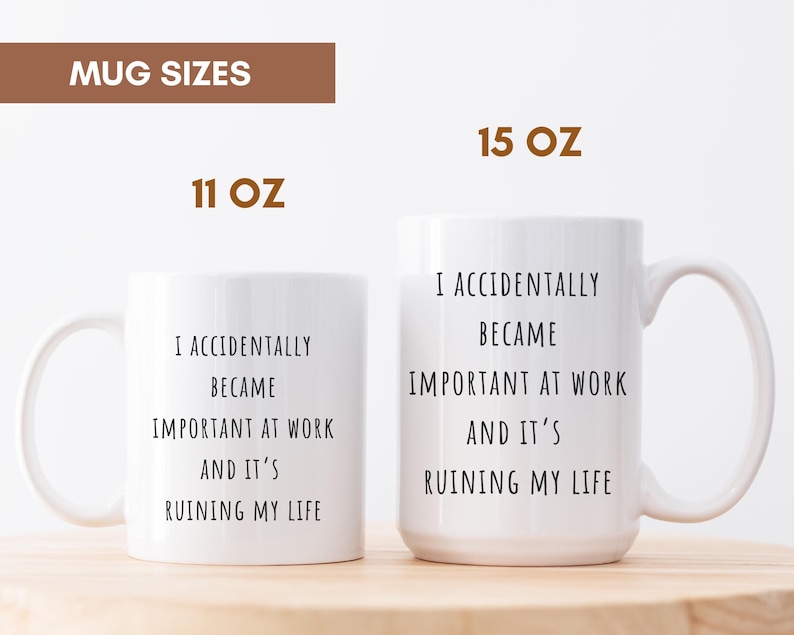 May include: Two white ceramic mugs, 11 oz and 15 oz, with the text "I ACCIDENTALLY BECAME IMPORTANT AT WORK AND IT'S RUINING MY LIFE" in black. The mugs have a curved handle and are on a light brown surface.