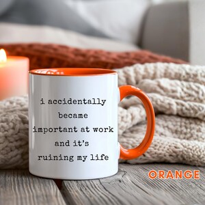May include: White ceramic mug with an orange interior and handle. The mug features the text "i accidentally became important at work and it's ruining my life" in black. The word "ORANGE" is written in orange at the bottom right.