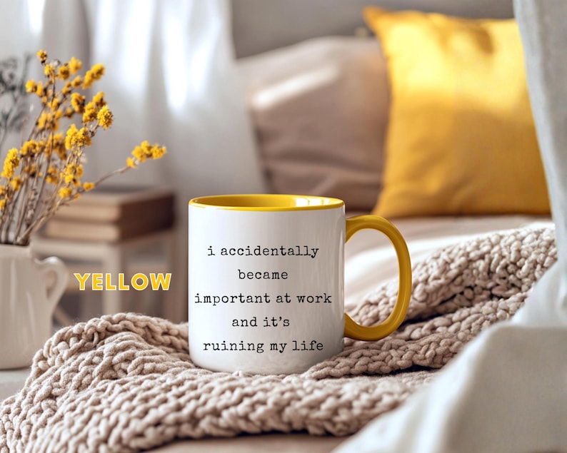 May include: White ceramic mug with a yellow interior and handle. The mug features the text "i accidentally became important at work and it's ruining my life" in black lettering. The mug is on a beige knitted blanket.