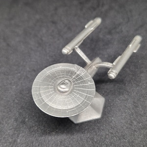 Puede incluir: Un modelo de plata de estaño de la nave espacial USS Enterprise de Star Trek. El modelo está detallado con una sección de platillo, nacelas y un plato deflector.