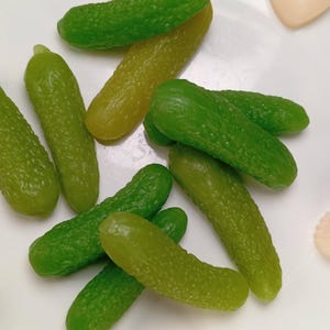 Può includere: Primo piano di un piatto di cetrioli sottaceto verdi all'aneto. I cetrioli sono disposti in modo casuale sul piatto bianco.