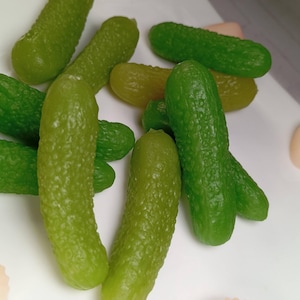 May include: A group of green and yellow pickle-shaped sweets. The sweets are arranged on a white surface.