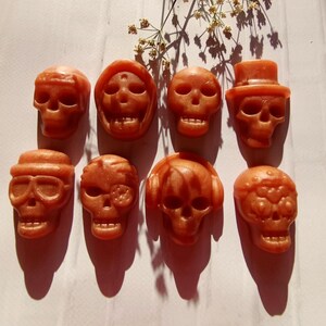 Puede incluir: Ocho adornos de resina en forma de calavera de color naranja con diferentes diseños. Las calaveras tienen varios detalles, incluyendo gafas, auriculares y un sombrero de copa.
