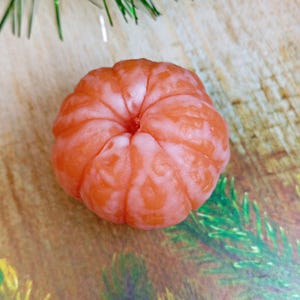 May include: A close-up of a peeled mandarin orange, showing the segments and the orange flesh. The orange is on a wooden surface with green pine needles.