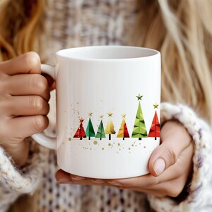 以下が含まれることがあります： 白いセラミック製のマグカップ。カラフルな幾何学模様のクリスマスツリーと金色の星が白い背景に描かれています。
