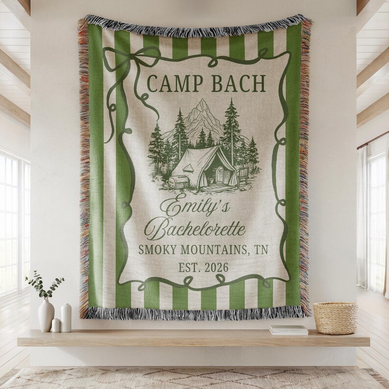 May include: A woven tapestry with green stripes and fringe. The center features a camping scene with a tent, trees, and mountains, along with the text "Camp Bach" and "Emily's Bachelorette, Smoky Mountains, TN, EST. 2026."