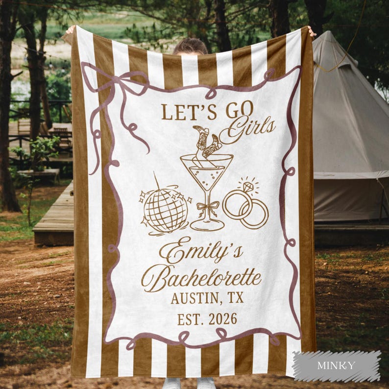 May include: A brown and white striped blanket with the text "LET'S GO Girls" and "Emily's Bachelorette AUSTIN, TX EST. 2026". The blanket features illustrations of a cocktail, disco ball, and rings.