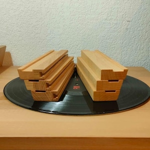 Peut inclure: Plusieurs blocs de bois brun clair avec un design rainuré, posés sur un disque vinyle noir. Les blocs sont disposés en deux groupes, mettant en valeur leur construction et leur texture. Le fond est un mur neutre.