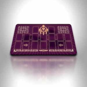 Pode incluir: Tapete de jogo retangular roxo com um design dourado. O tapete de jogo apresenta um emblema central, zonas de cartas e padrões decorativos. O design inclui formas geométricas e texto estilizado, adequado para jogos de cartas.