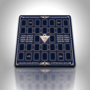Puede incluir: Una alfombrilla de juego rectangular azul con un borde dorado y un patrón de cuadrícula. El centro presenta un triángulo dorado con un símbolo de ojo. La alfombrilla tiene espacios para cartas y texto decorativo de estilo jeroglífico.