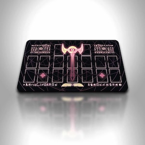 Op de afbeelding: Een zwarte rechthoekige speelmat met een roze en gouden ontwerp. Het ontwerp toont een oogsymbool met tekst in hiërogliefenstijl en rasterpatronen. De speelmat is ontworpen voor kaartspellen.