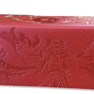 Könnte beinhalten: Rote rechteckige Box mit geprägten Kunstwerken. Die Box zeigt eine detaillierte Illustration eines Charakters mit fließendem Haar und einem Schwert. Goldakzente sind auf der Oberseite sichtbar. Die Box dient wahrscheinlich zur Aufbewahrung.