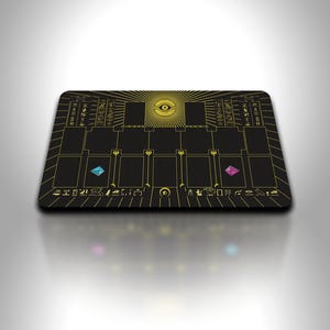 Puede incluir: Alfombrilla de juego rectangular negra con un diseño de ojo dorado y símbolos de estilo jeroglífico. La alfombrilla presenta zonas de cartas y dos gemas de colores. El diseño del ojo está centrado, con rayos de sol que emanan de él.