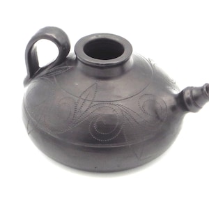 Peut inclure: Une théière en céramique noire avec un corps rond et un petit bec verseur. La théière a une poignée et est décorée d'un motif de volutes et de lignes.