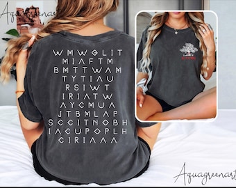 May include: A dark gray t-shirt with a white graphic of a tree with the text "Friends of All Creatures" on the front. The back of the shirt has a white graphic of a grid of letters that spell out "FRIENDS OF ALL CREATURES".