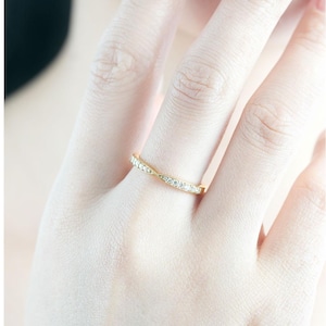 Op de afbeelding: Een gouden bandring met kleine, heldere edelstenen. De ring zit aan de vinger van een persoon, met de hand en een deel van het gezicht zichtbaar. De ring heeft een delicaat, elegant ontwerp.