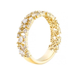 May include: A gold-colored ring with a double band design. The top band is adorned with numerous clear, sparkling gemstones of varying sizes and shapes. The ring's band has an open, decorative filigree pattern.