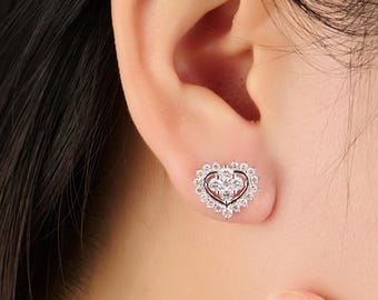 May include: A close-up of a heart-shaped stud earring. The earring features a cluster of clear gemstones at the center, surrounded by a halo of smaller gemstones. The earring is set in a silver-colored metal.