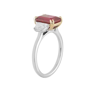 May include: A silver ring with a large, rectangular, deep red gemstone and a smaller, white, rectangular gemstone. The setting has gold accents. The ring is set against a white background.