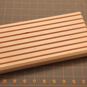 Puede incluir: Una bandeja de madera con ocho ranuras paralelas, ideal para organizar y exhibir objetos peque&ntilde;os.