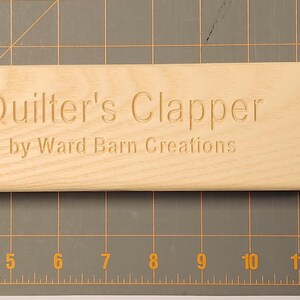 Peut inclure: Un batteur de quilting en bois clair avec le texte "Quilter's Clapper by Ward Barn Creations" grav&eacute; sur la surface.