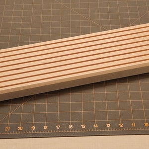 Puede incluir: Una tabla de madera con una serie de ranuras paralelas cortadas en la superficie. Las ranuras est&aacute;n te&ntilde;idas de un color marr&oacute;n rojizo, mientras que el resto de la tabla es de color madera claro.