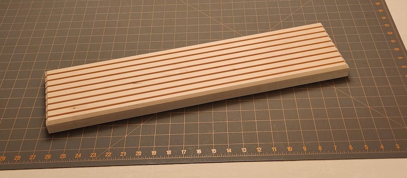 Puede incluir: Una tabla de madera con una serie de ranuras paralelas cortadas en la superficie. Las ranuras est&aacute;n te&ntilde;idas de un color marr&oacute;n rojizo, mientras que el resto de la tabla es de color madera claro.
