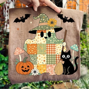 Pode incluir: Uma almofada decorativa castanha com tema de Halloween com um fantasma de patchwork usando um chapéu de bruxa com um girassol. O design inclui um gato preto com gravata borboleta, uma abóbora esculpida e morcegos.