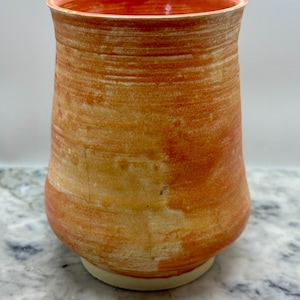 May include: Handmade ceramic vase with a textured surface. The vase features a warm color palette of orange and cream, with a slightly flared rim and a rounded base. The interior rim is a darker shade of orange.