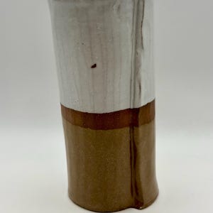 May include: A handmade ceramic vase with a two-tone design. The top half is white, the middle has a brown band, and the bottom is brown. The vase has a slightly irregular shape and a glossy finish, perfect for displaying flowers or as a decorative piece.