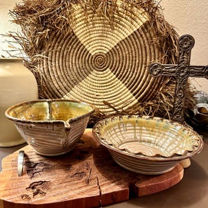 May include: Two ceramic bowls with a brown and white striped glaze and a yellow glaze on the rim. The bowls are sitting on a wooden cutting board with a metal handle.