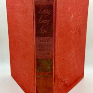 May include: A vintage book titled "Long, Long Ago" with a red cover and spine. The spine features the title and author's name in gold lettering. The book's cover shows signs of wear, suggesting its age.