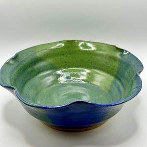 May include: A handmade ceramic bowl with a wavy rim. The bowl is glazed in shades of green and blue.