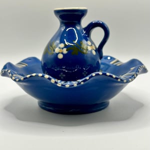 May include: A blue ceramic pitcher with white flowers and green leaves sits inside a blue ceramic bowl with a scalloped edge and white dots.