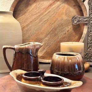 Könnte beinhalten: Ein Set aus brauner und weißer glasierter Keramik für die Küche. Das Set enthält einen Milchkännchen, eine kleine Schüssel mit zwei einzelnen Dipschüsseln und eine größere Schüssel. Die Schüsseln haben eine braune und weiße Glasur mit einem gesprenkelten Muster.