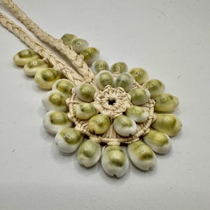 May include: A white and green shell necklace with a woven cord and a large cluster of shells in the center.