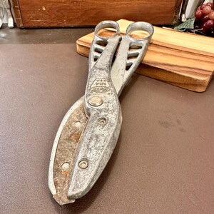 May include: Vintage metal shears with a silver finish and two finger holes. The blades are slightly rusted, and the tool has the text "M14 U.S.A." stamped on it. The shears are designed for cutting and are likely used for gardening or crafting.