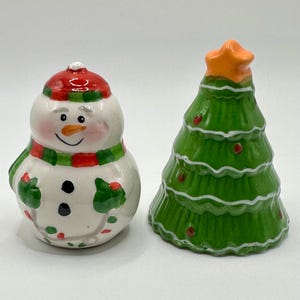 May include: A ceramic snowman salt and pepper shaker set. The snowman is wearing a red and green hat and scarf. The pepper shaker is a green Christmas tree with a star on top.