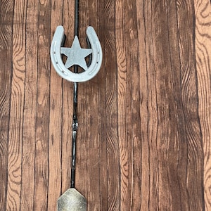 May include: A metal arrow with a horseshoe and a star at the center, mounted on a wooden background.