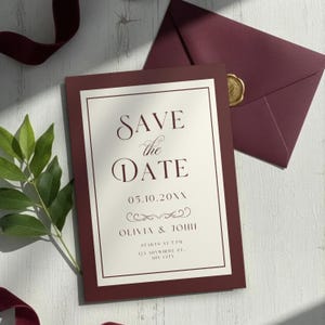 May include: Burgundy Save the Date card with a cream-colored interior and elegant script. The card reads "SAVE the DATE" with the date, names, and event details. A matching envelope with a gold wax seal is also present.