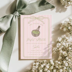 Puede incluir: Una tarjeta de invitación a rayas rosas y blancas con el texto "She Found Her Perfect Matcha". La tarjeta presenta un cuenco de matcha con un batidor, un lazo y detalles florales. La invitación es para un evento nupcial.