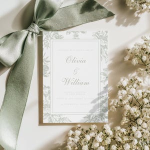 May include: A wedding invitation featuring the names "Olivia & William" in elegant script. The invitation has a floral design in a soft green hue, framed by a white border. A sage green ribbon and white flowers accent the invitation.