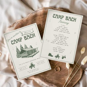 May include: Two cream-colored Camp Bach themed invitation cards with green text and illustrations. One card says "You're invited to Camp Bach" and the other is a detailed itinerary. The cards are on a wooden surface.