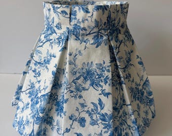 May include: A lampshade with a pleated design, featuring a white background and a blue floral pattern. The shade has a flared shape and is made of fabric. The floral design includes roses and other flowers.