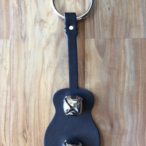 May include: A black leather guitar-shaped door knocker with two silver bells.